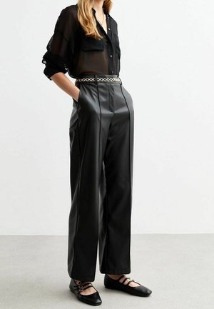 Černá průsvitná košile na knoflíky se dvěma náprsními kapsami, kombinovaná s černými kalhotami širokého střihu z umělé kůže s vysokým pasem a černými plochými botami.