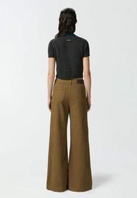 Sivi kratki pulover s prilegajočim se krojem. Hlače v bež barvi s širokimi nogavicami in teksturirano površino ter zadnjimi žepi, opremljene z majhnim logotipom.