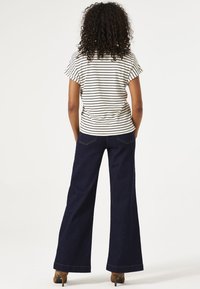 Camisa de manga corta a rayas en crema y negro, combinada con unos vaqueros de pierna ancha de cintura alta en azul oscuro. Unos zapatos marrones de tacón completan el look.