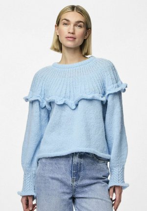 Pull en maille bleu clair avec un ourlet froncé, des poignets larges et un motif texturé. Associé à un jeans en denim bleu clair.
