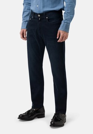 Dark blue denim jeans with a straight cut, five-pocket design, and a button closure. Paired with black leather shoes and a light blue shirt.