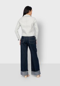 Weiße Lederjacke mit tailliertem Design, kombiniert mit dunkelblauen, weit geschnittenen Jeans mit hochgekrempeltem Saum und zwei Gesäßtaschen.