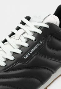 Ténis de couro preto com atacadores brancos e língua branca. Apresenta logo em relevo do lado e sola texturizada para aderência.