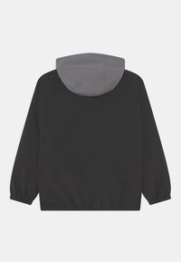 Veste noire avec capuche grise, dotée de poignets élastiques et d'un ourlet avec cordon de serrage, fabriquée dans un tissu lisse et léger. Design minimaliste.