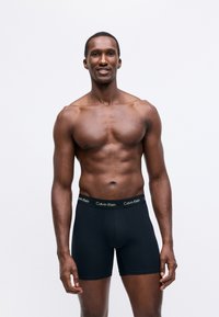Fekete boxer alsónadrág puha anyagból, Calvin Klein logós derékszíjjal, szoros illeszkedéssel és sima textúrával tervezve.
