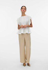 Witte, textured peplumtop met korte, gerafelde mouwen, gecombineerd met beige, wijde broekspijpen en spitse, gemusterde schoenen.