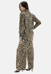 Mono de leopardo en tejido suave; cuenta con mangas largas, cuello con solapa, piernas anchas y un detalle anudado en la cintura.