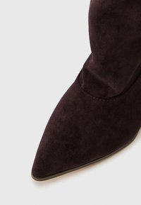 Pointed-toe ankle boot made of dark purple suede, featuring a smooth texture and a stitched seam along the upper edge.