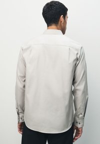 Light gray long-sleeve shirt with a textured pattern, buttoned cuffs, and a rounded hem. Features a classic collar and straight back design.