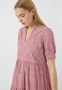 Pink cotton dress with a V-neck, puff sleeves, intricate cut-out patterns, and a tiered skirt, featuring embroidery and scalloped edges.