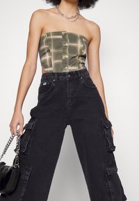 Grön rutig off-shoulder topp med framsida knappar, ihop med svarta cargobyxor med sidofickor och en silverkedjeväska.