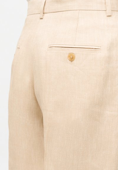 Μπεζ λινό παντελόνι με πίσω τσέπη τύπου welt που ασφαλίζεται με ένα καφέ κουμπί και θηλιές ζώνης στη μέση.