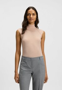 Light beige sleeveless turtleneck top made of soft material, paired with tailored gray trousers featuring pockets and a straight cut.