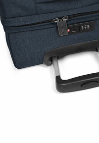 Valigia a rotelle blu scuro con un esterno in tessuto texturizzato, doppia zip, lucchetto a combinazione e manico retrattile con una presa robusta.