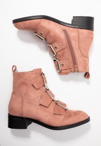 Růžové semišové kotníkové boty s kulatou špičkou, bočním zipem a třemi dekorativními popruhy se sponami. Nízký blokový podpatek a strukturovaný povrch.