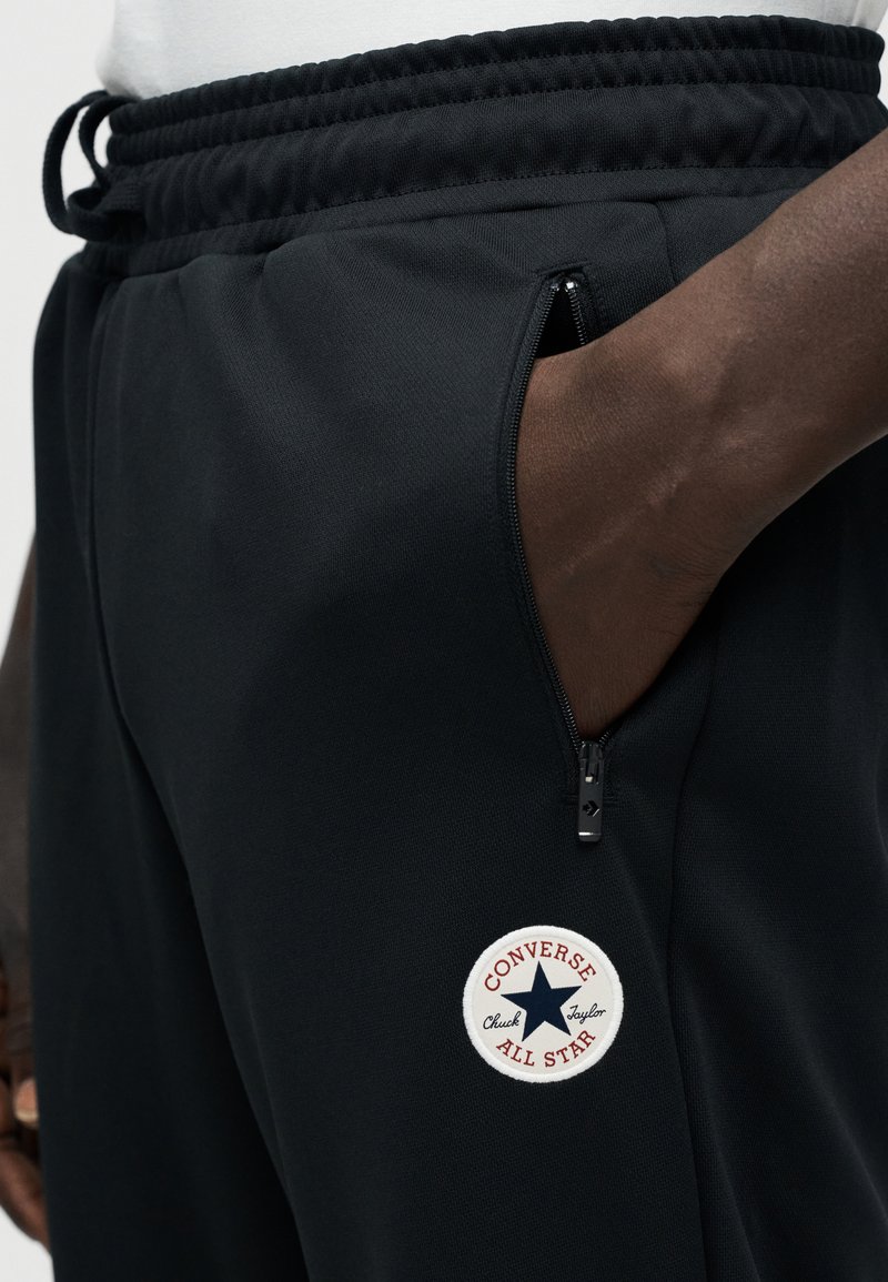 Sorte sweatpants med en struktureret finish, med en lynlåslomme og et hvidt rundt logopatch med røde og blå accenter.