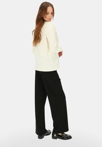 Kremowa bluzka z długim rękawem, luźny krój, fakturowana tkanina; szerokie czarne spodnie, gładka tkanina, pełna długość; błyszczące czarne mokasyny ze złotymi akcentami.