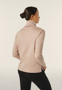 Top a maniche lunghe rosa chiaro con collo a imbuto in tessuto morbido e elasticizzato. Presenta una vestibilità rilassata e fessure laterali all'orlo. Indossato con pantaloni neri.