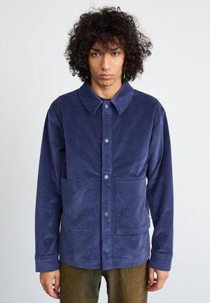 Navy blue corduroy shirt jacket with a button front, large chest pocket, and pointed collar. Soft texture, relaxed fit.
