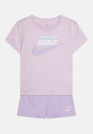 Camiseta de algodón morada con manga corta y logo de Nike en rayas azules y blancas. Combinada con pantalones cortos morados a juego que presentan un pequeño logo.