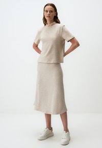 Haut en tricot beige à manches courtes et col montant, assorti d'une jupe longue jusqu'à la cheville, complété par des baskets blanches.