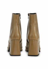 Brūnie ādas potīšu zābaki ar augstu bloku papēdi, ar rāvējslēdzēja aizdari un gludu tekstūru. Šuvju detaļa aizmugurē.