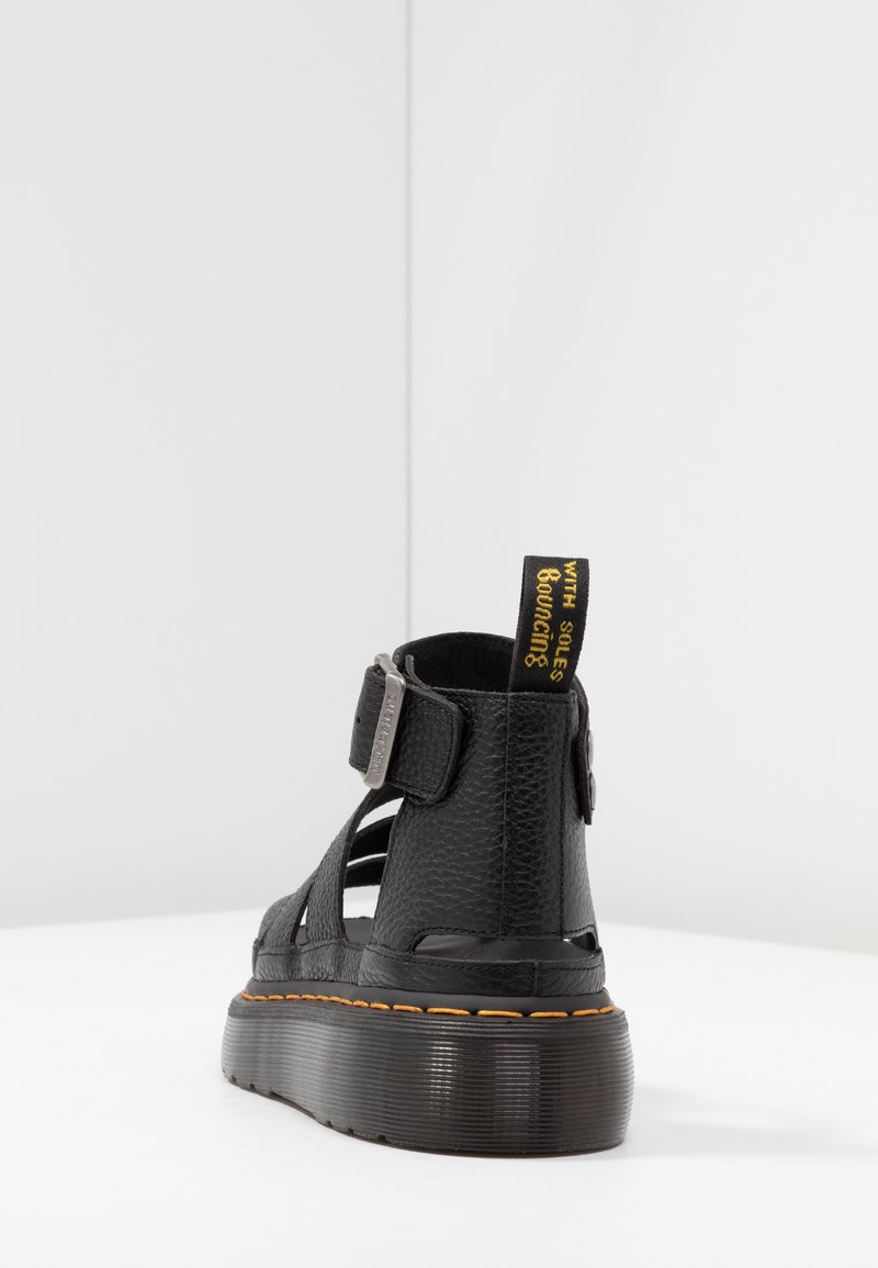 Black sandal with textured leather, open sides, adjustable strap, and rubber sole. Features a black and yellow pull tab.