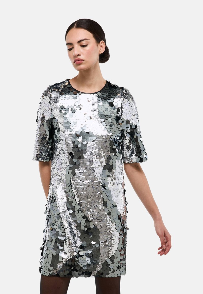 Robe à manches courtes couverte de sequins argentés et gris, avec une coupe ample et un col rond, présentant une texture lisse et une finition brillante.
