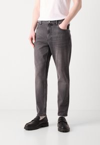 Grå denimjeans med avslappnad passform, femficksdesign och en lätt blekt textur. I kombination med svarta skor och en vit skjorta.