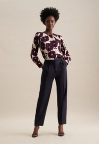 Blusa a maniche lunghe con base crema e grande stampa floreale bordeaux, abbinata a pantaloni dritti navy e sandali neri con tacco.
