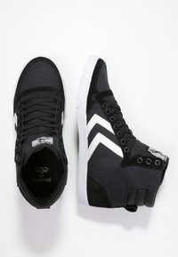 Black high-top sneakers featuring a mix of canvas and suede materials, with white chevron accents and a rubber sole.