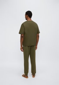 Σετ άνετης βαμβακερής ρούχας σε ελιάς πράσινο χρώμα που αποτελείται από μία κοντομάνικη μπλούζα και παντελόνι με άνετη γραμμή. Απλός σχεδιασμός με χαλαρή σιλουέτα.