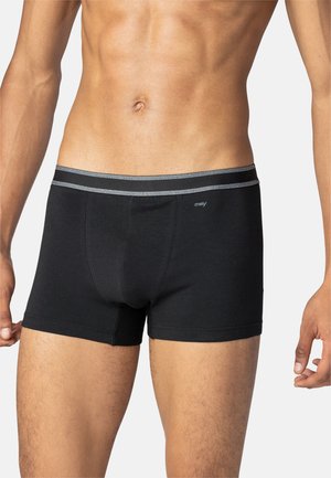 Torace maschile che indossa boxer neri con fascia elastica grigia e piccolo logo "mey" sull'anca sinistra su sfondo neutro.