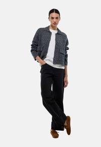 Veste en maille texturée grise au design court, dotée de deux poches avant. Associ ée à un jean large noir et des chaussures marron.