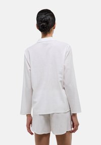 Ensemble de leisure en lin blanc comprenant un haut à manches longues avec col et un short assorti avec des ourlets en forme de vagues. Tissu texturé pour une meilleure respirabilité.