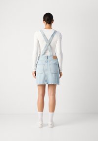 Lyseblå denim overallkjole med justerbare stropper, lommer bak, rå kant, og et vevd merke på midjebåndet.