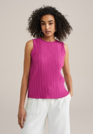 Fuchsia mouwloze top van textuurstof met geplooid materiaal, ronde halslijn en een relaxte pasvorm, gecombineerd met lichte, wijde witte broek.