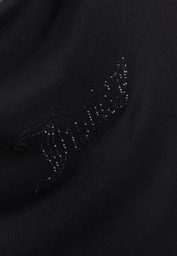 Mustast kangast top, millel on kootud sädelev logo kursiivkirjas. Materjal tundub sile ja õrnalt läikiv.