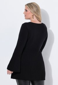Schwarzer Pullover aus geripptem Stoff mit ausgestellten Ärmeln, der einen enganliegenden oberen Teil und einen strukturierten unteren Saum hat.