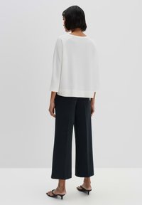 White ribbed sweater with three-quarter sleeves, paired with wide black pants. Minimalist design, soft texture, and relaxed fit.