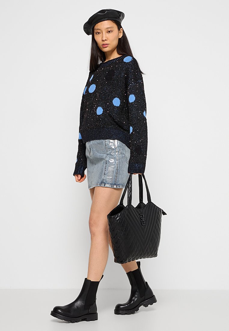 Pull noir à pois bleus, associé à une jupe en denim argentée, des bottines Chelsea noires et un sac fourre-tout noir à motifs.