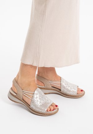 Beige open-toe sandals with a textured silver geometric design, featuring a cushioned sole and crisscross straps for support.