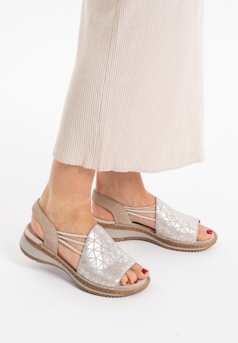 Beige open-toe sandals with a textured silver geometric design, featuring a cushioned sole and crisscross straps for support.
