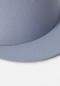 Lys blå hatt med en teksturert overflate som har et lite rutenettmønster. Bred skjerm og glatt finish som fremhever det lette stoffet.