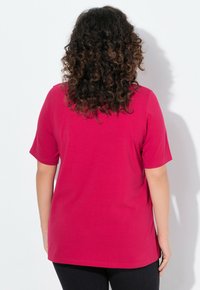 T-shirt fuchsia à manches courtes en tissu doux, avec une coupe décontractée et un col rond. La vue de dos montre des cheveux texturés et bouclés sur fond blanc.