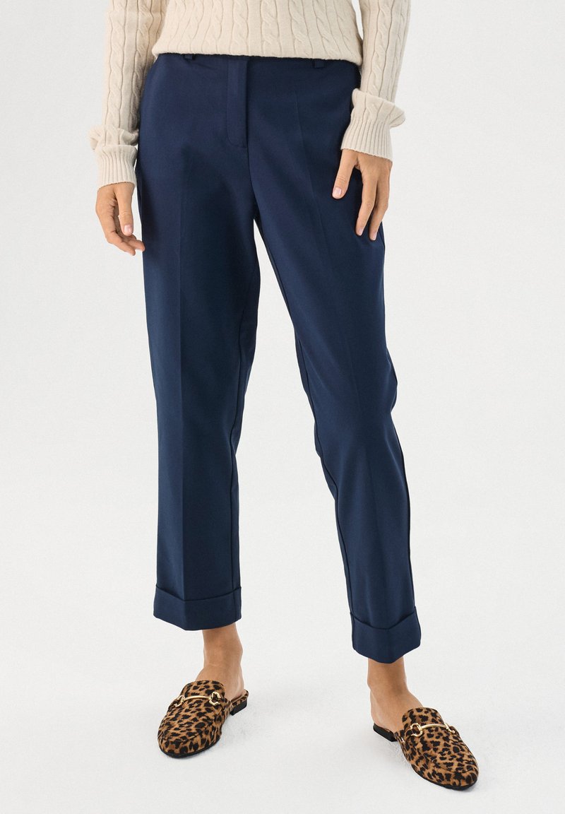 Pantalons tailleur bleu marine en tissu lisse, avec une jambe droite, un ourlet à revers et des plis sur le devant. Associés à des chaussons imprimé léopard.