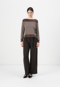 Maglione a strisce marroni con scollatura ampia abbinato a pantaloni neri a gamba larga. L'outfit presenta un tessuto testurizzato e una vestibilità rilassata.