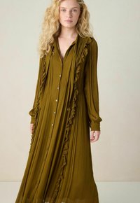 Robe olive, à manches longues, avec un devant à boutons, des accents volants le long des côtés et un tissu fluide et texturé.