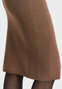 Jupe en tricot marron avec une texture à côtes verticales, longueur au genou et une finition en tissu lisse. Convient pour un port décontracté ou semi-formel.