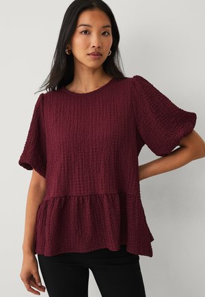 Burgundy textured blouse with short puff sleeves, featuring a peplum hem and a round neckline, made of a crinkled fabric.